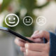 Participación en una encuesta de satisfacción: Una persona sostiene un celular y utiliza emoticonos para calificar su experiencia en una encuesta de satisfacción del servicio.